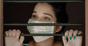Women with facemask staring out behind bars