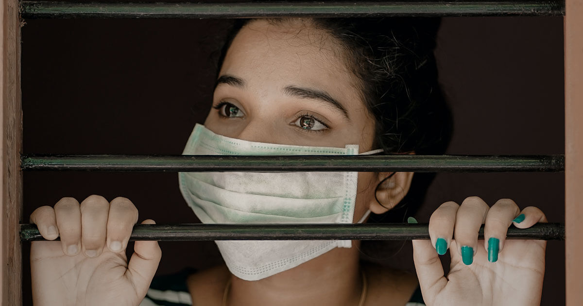 Women with facemask staring out behind bars